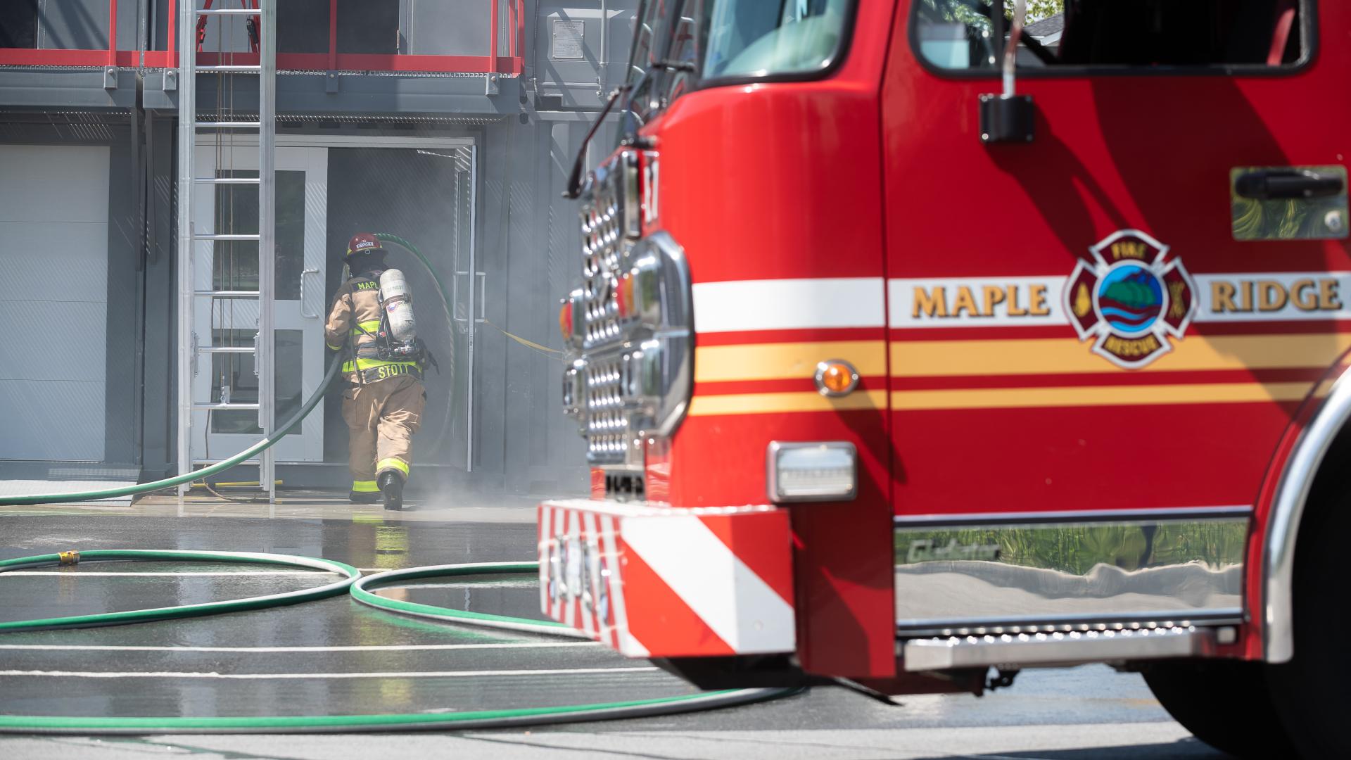 A fireman wielding a hose connected to a fire engine in the foreground enters an active blaze in a training facility at Fire Hall number 4.