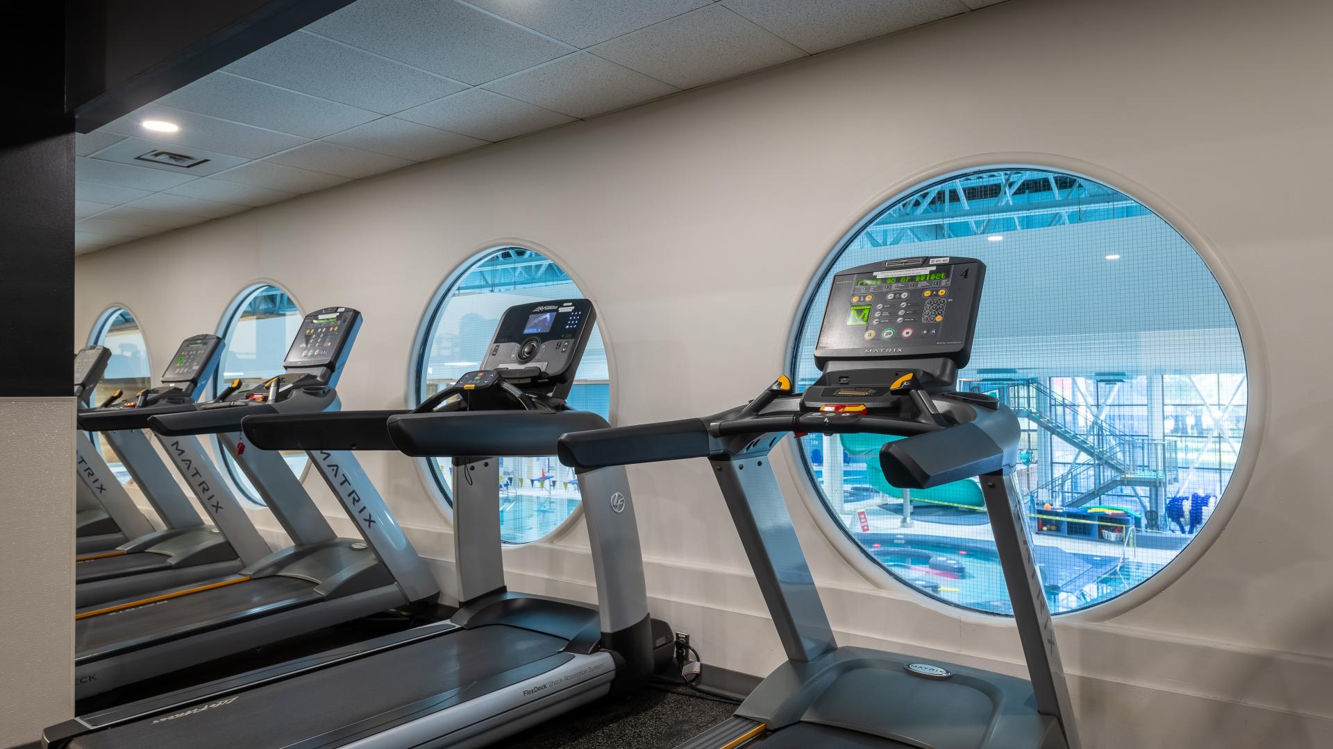 A line of treadmills on the second floor look out circular windows to the indoor pool on the first floor of the Maple Ridge Leisure Centre.