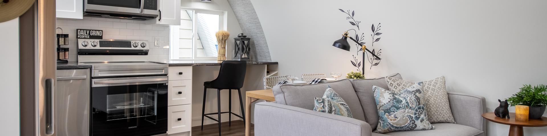 A stylish grey couch sits in front of a small kitchenette.