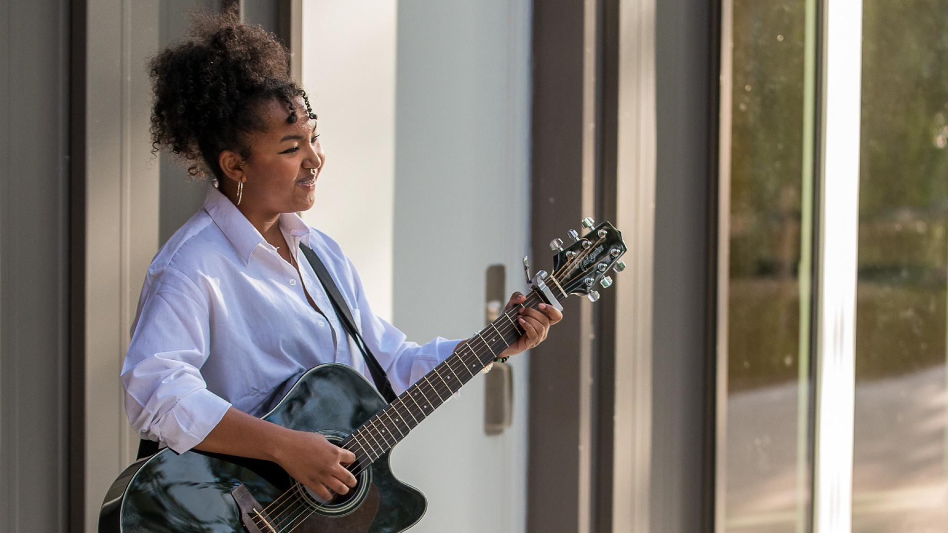 A woman holding a guitar sings along the side of the Albion Community Centre.