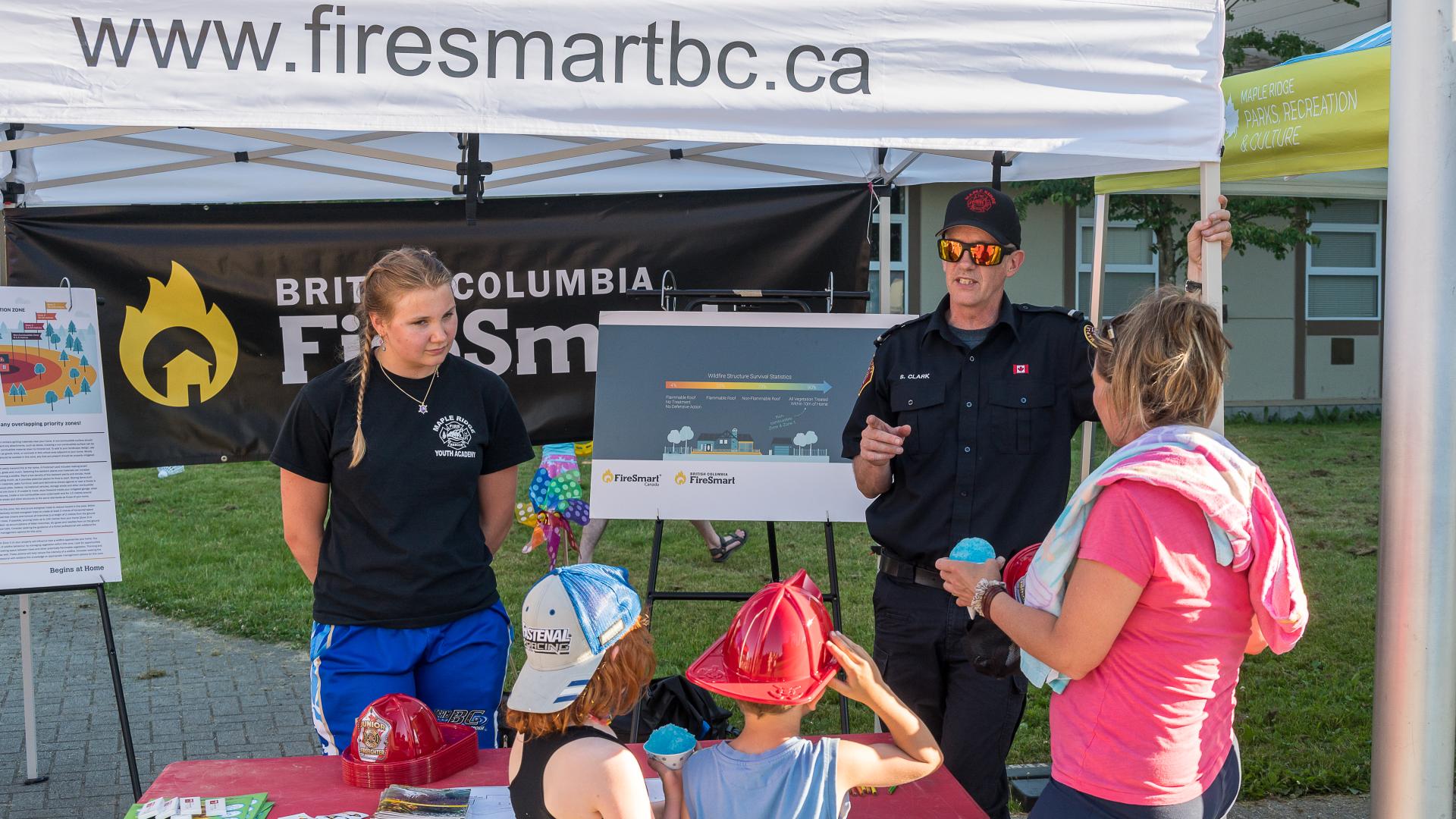 A pair of educators teach kids and their guardian about fire safety at a Fire Smart booth during a 2022 Hot Summer Nights event.