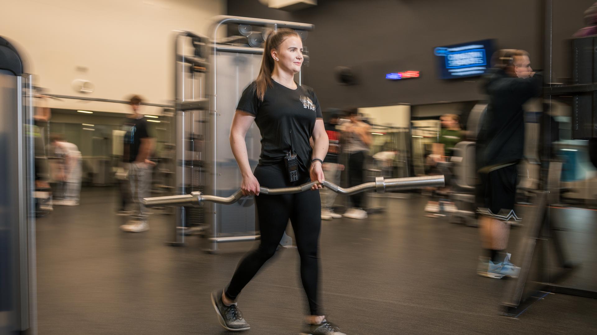 A female Maple Ridge Leisure Centre staff moves a weightlifting bar from one end of the facility to the other.