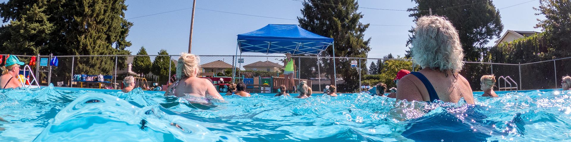 A group of senior citizens in the Hammond Outdoor Pool follow a poolside instructor's movements for an aquafit class.