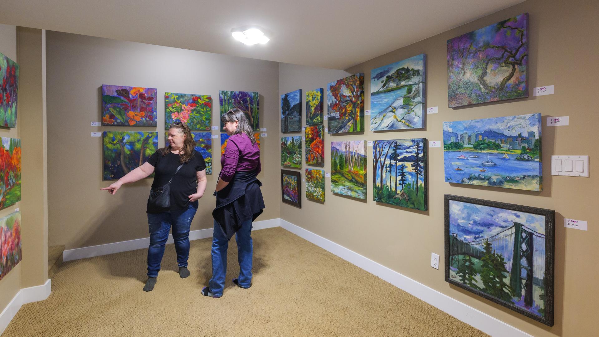 One woman points out an interesting painting to the woman next to her in a hallway lined with artwork.