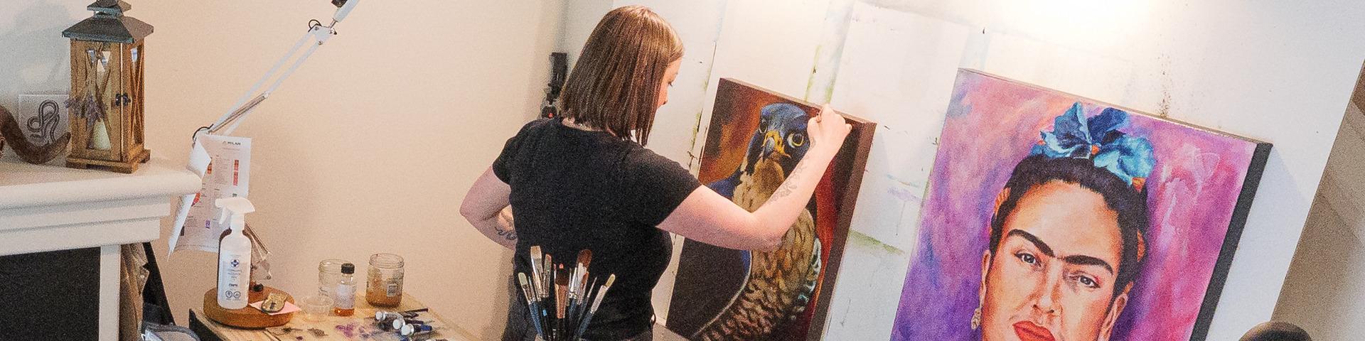 A woman reached up to put another brushstroke on a painting of a falcon.