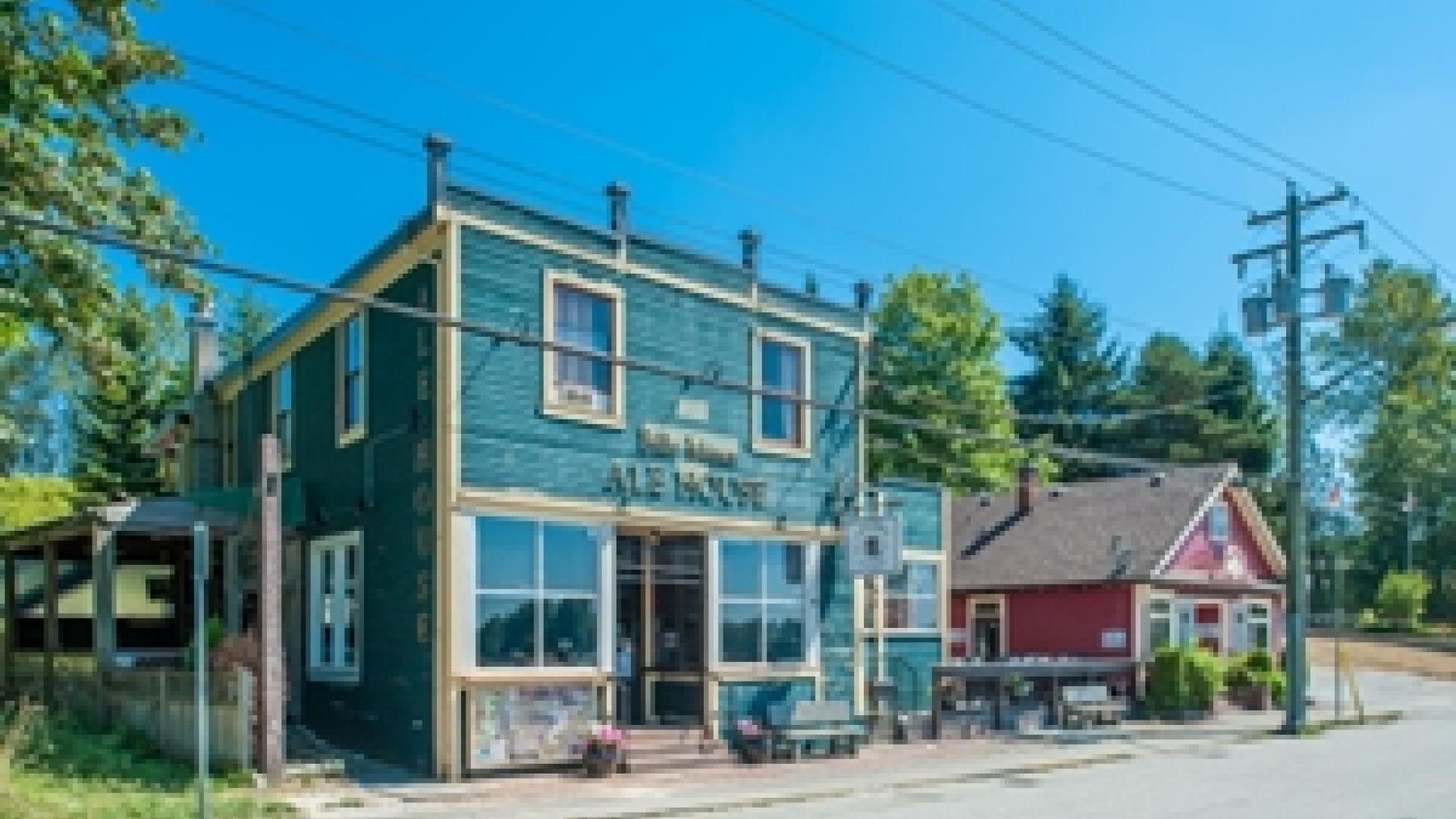 Exterior of old Bank of Montreal building. The bank is a blue, multi-story wooden building. The building is in front of a road.