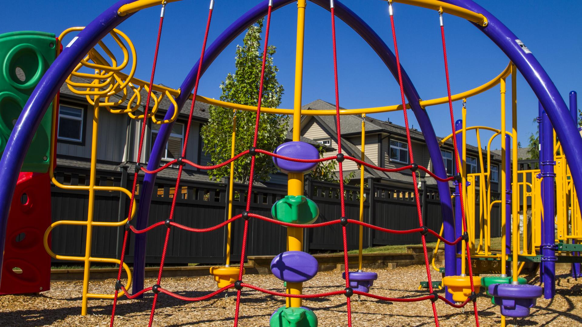 A large and bright climbing rope structure around other playground structures.