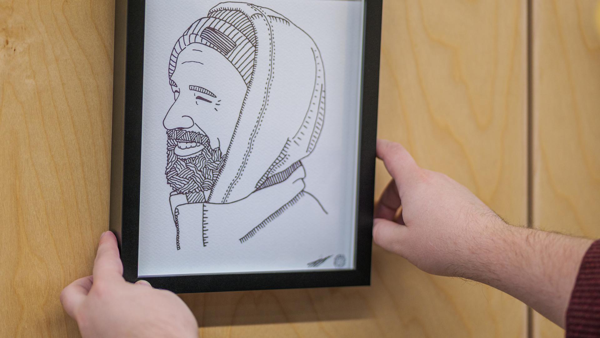 Alex Neff hangs one of many black-and-white line art portraits in their art installation, "Constellation".