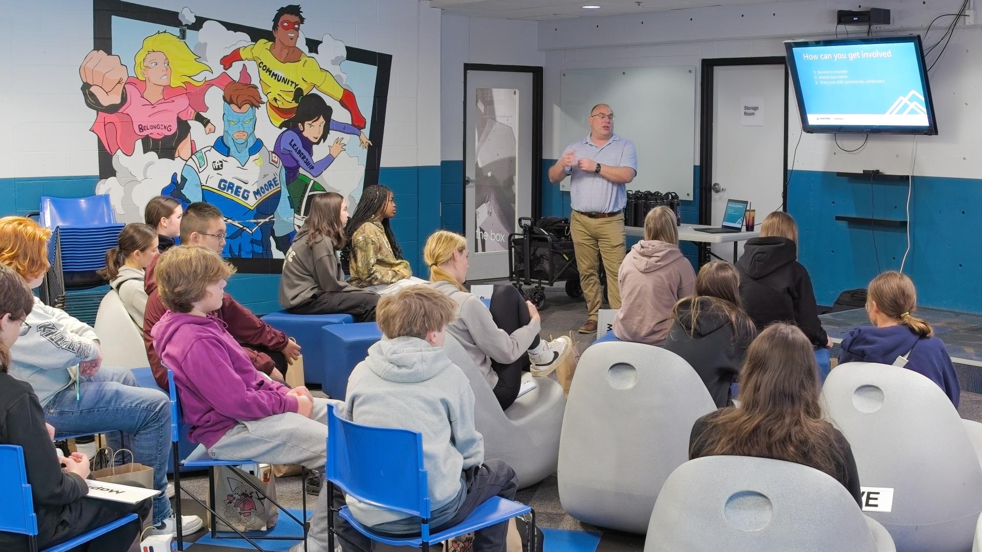 A man delivers a powerpoint presentation to a group of grade nine students.