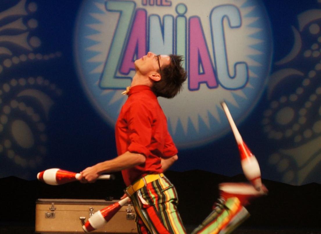 Alex Zerbe kicks a club while actively juggling while performing his Zaniac show.