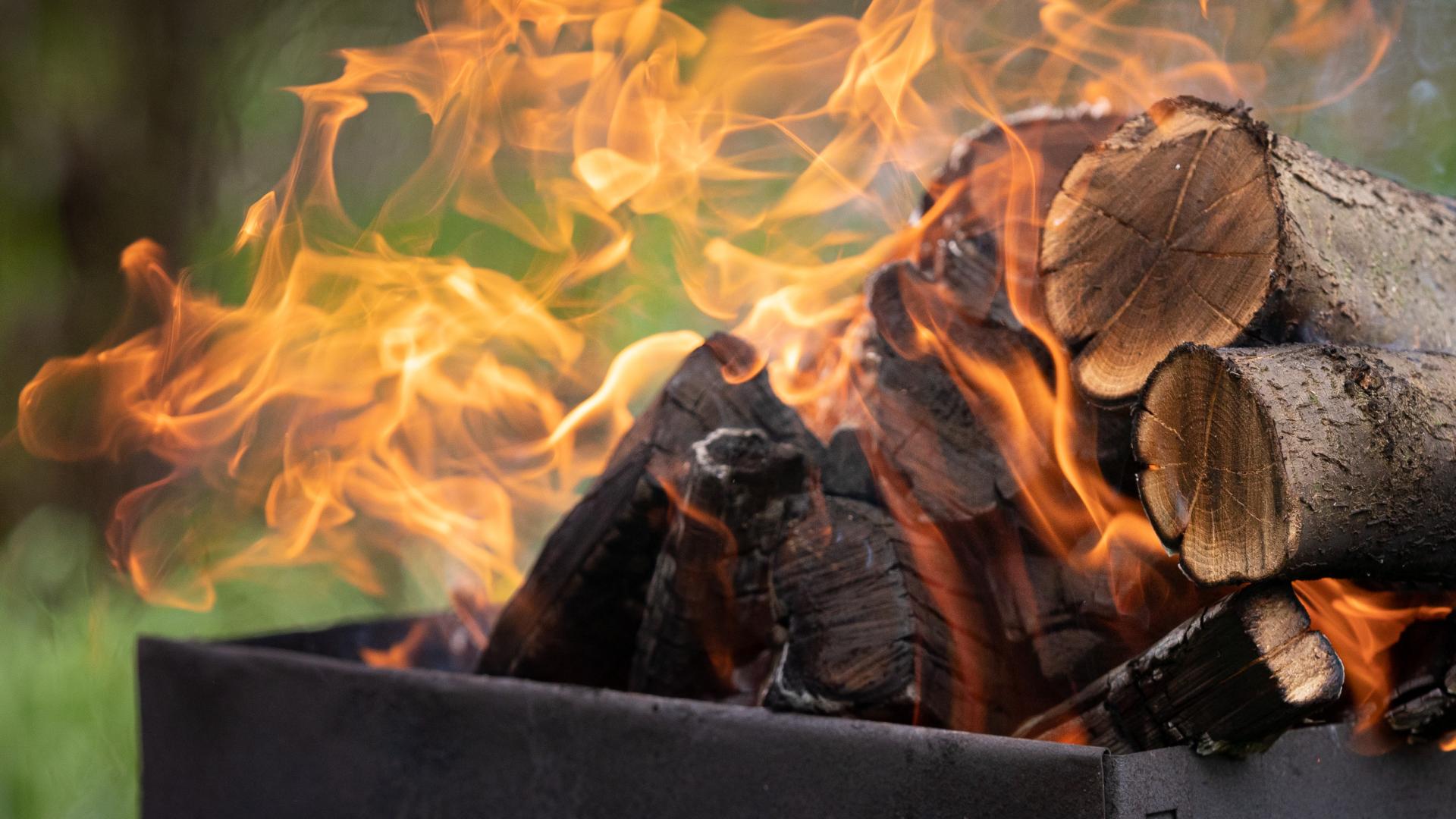 A pile of logs burn upon a raised campfire bed.