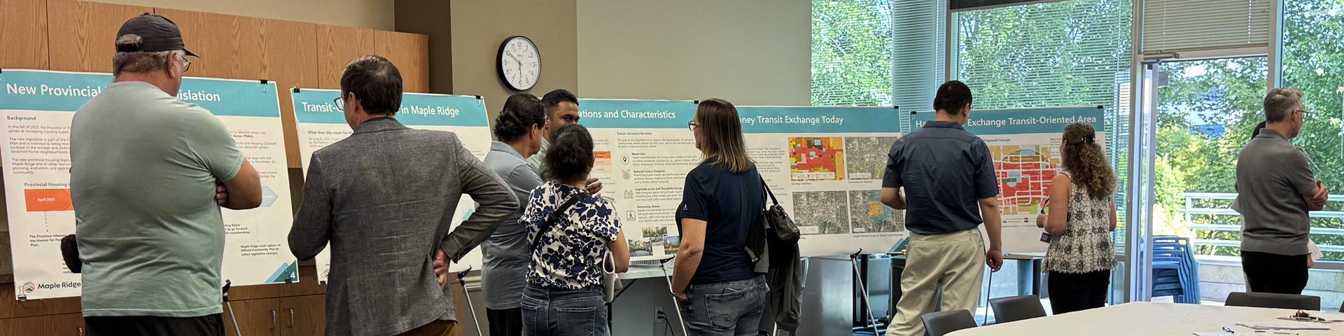A crowd of people review information on boards at a City open house.