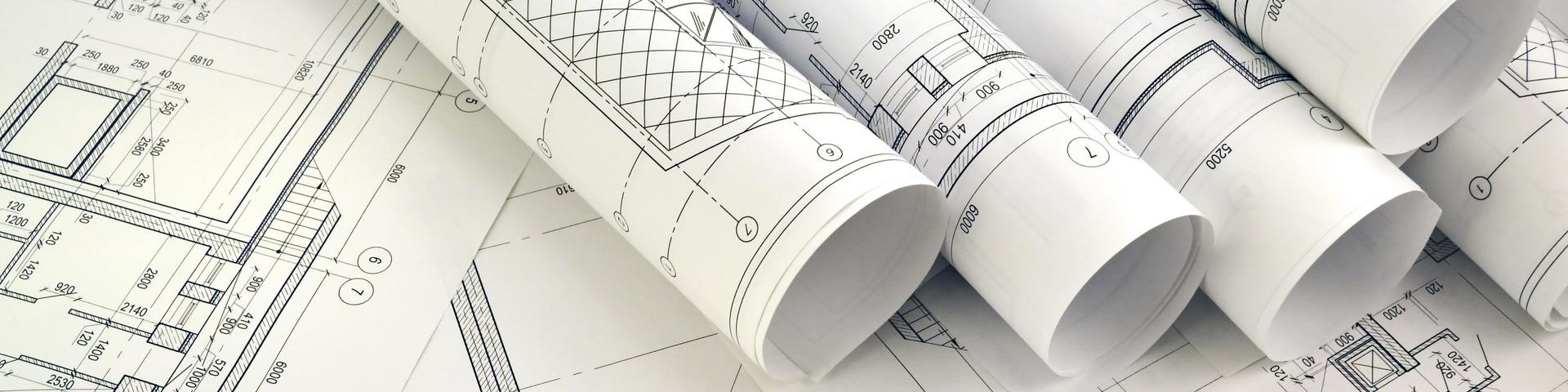 Rolled up white paper building plans sit on top of other flat plans.