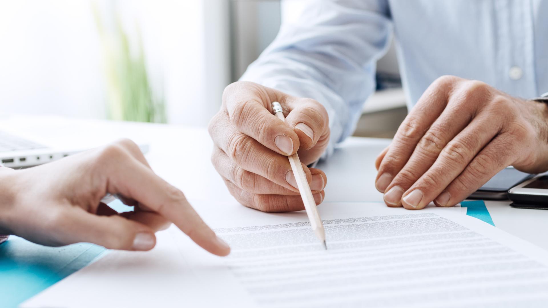 An individual points with their forefinger to a spot, while a second person points to the same location with a pen.