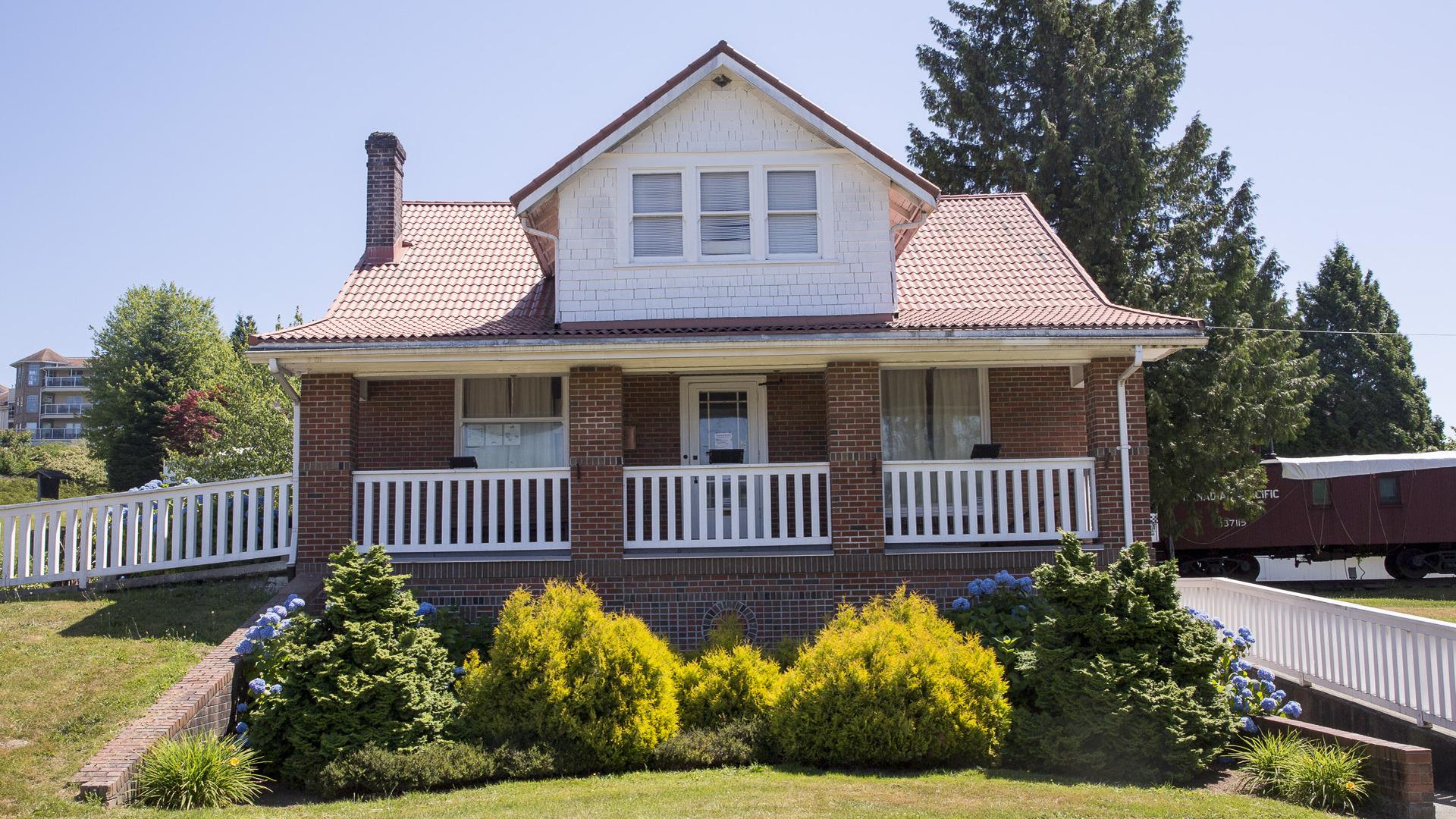 A large brick museum sits above a paved walkway lined with bushes next to a traincar.