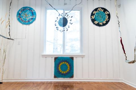 Large room with white wooden walls displaying different art pieces by Colleen Brown. The works of art consist of small pieces of shag carpet-like material. There are basic geometrical shapes in bright colours.