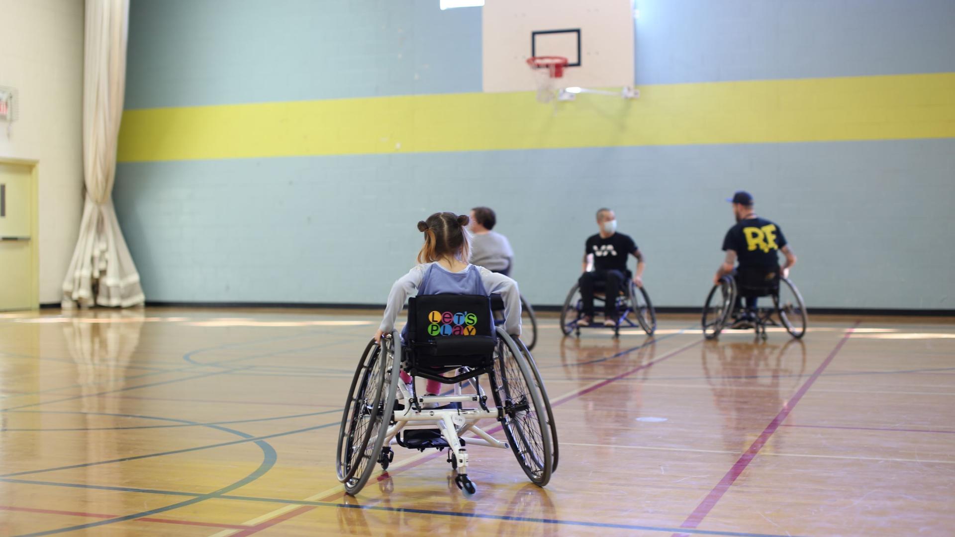 A young girl, viewed from behind, playing wheelchair basketball