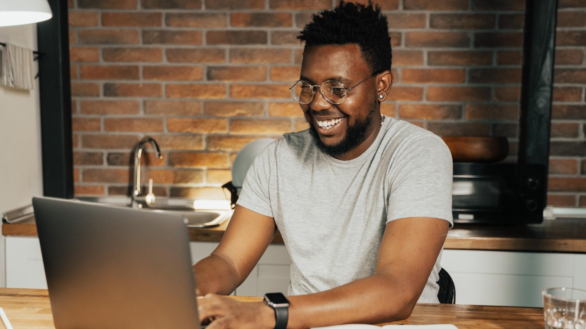 A man smiles as he types on his laptop computer.