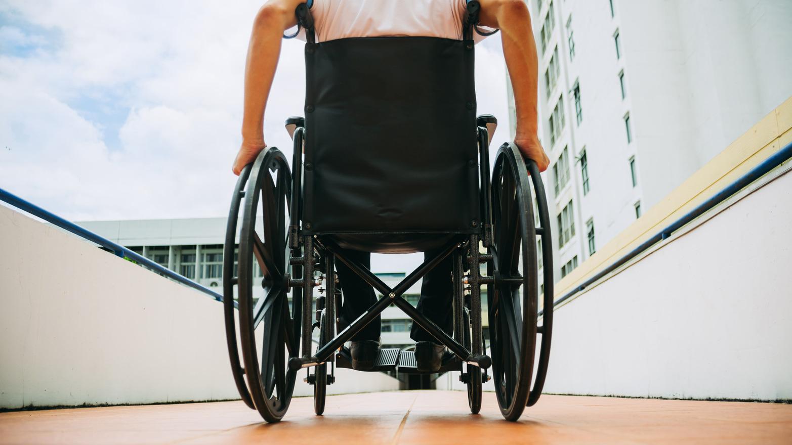 A person in a wheelchair travels down a ramp out of a building.