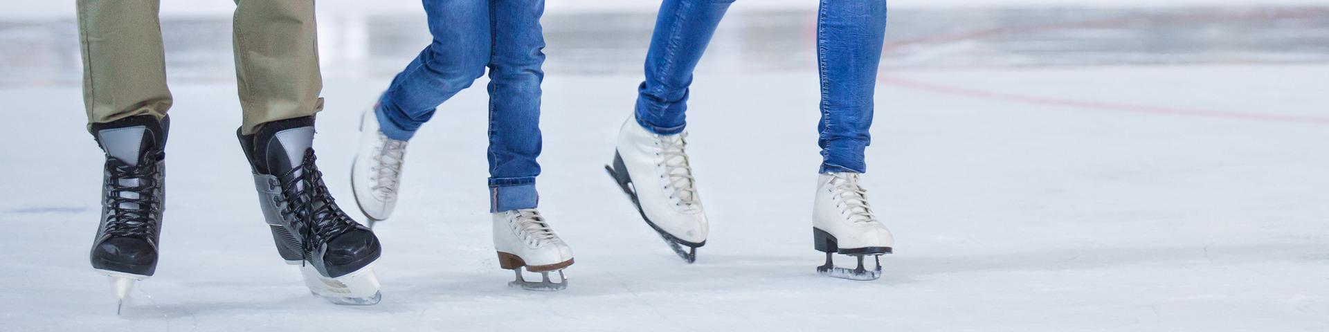 The legs and skates of two adults at an ice rink with a child glide across the white frosty surface.
