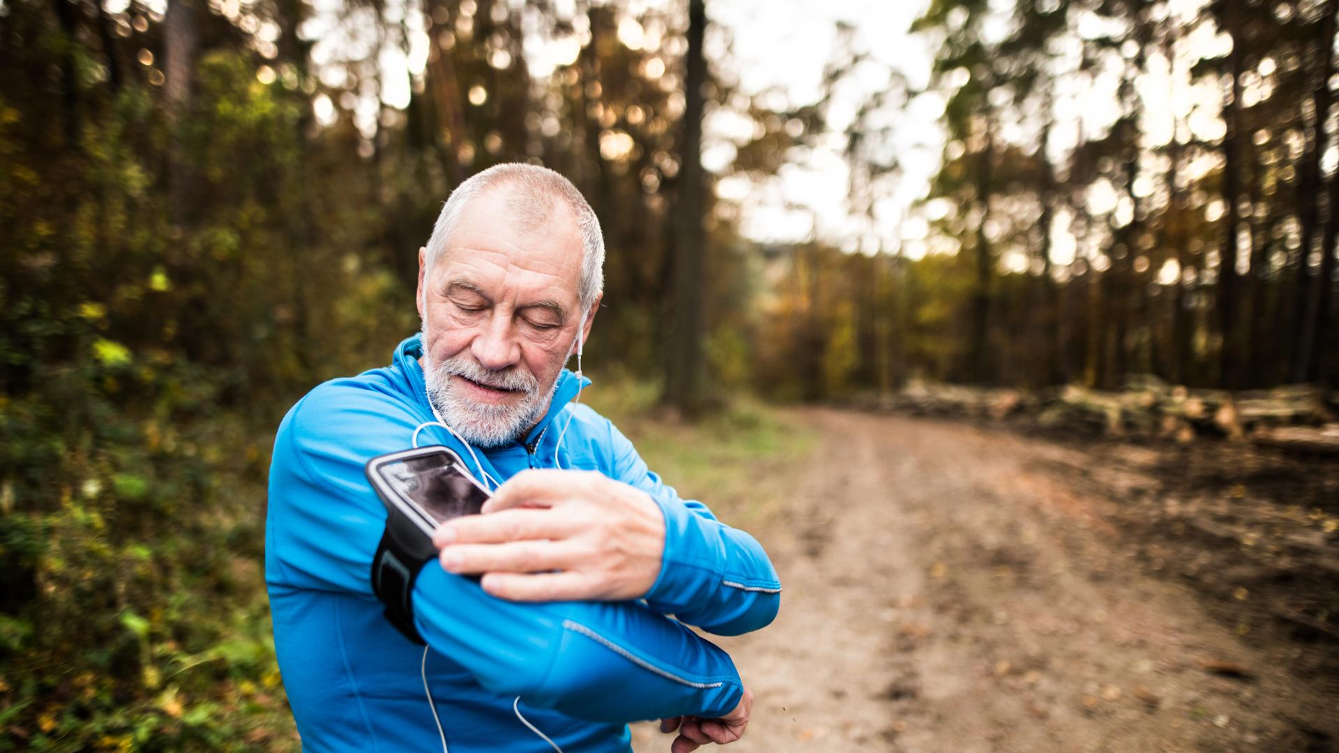 An older man checks a device strapped to his arm whilst hiking in a forest.