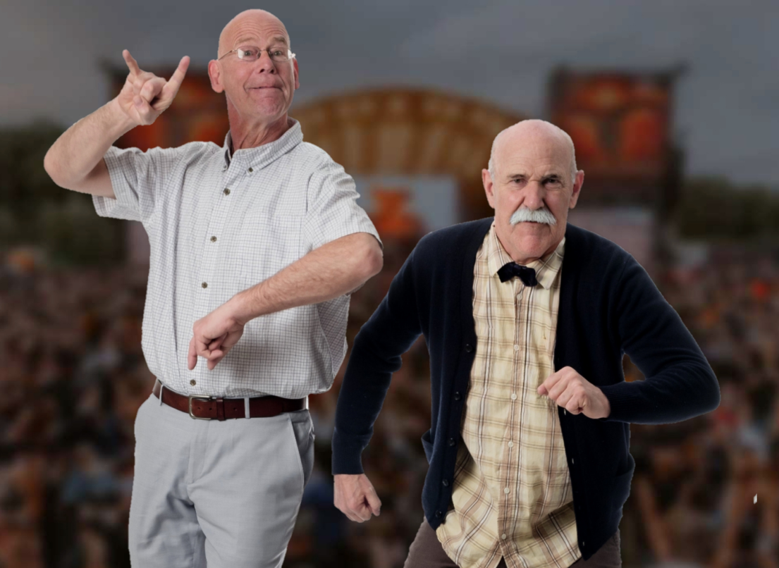 Two senior men pose in front of a concert backdrop, one of them making the "rock on" symbol with his right hand.