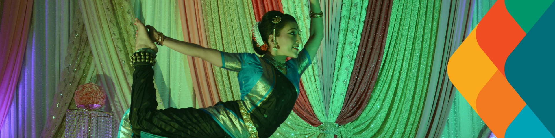 A dancer holds her foot in the air with her hand, reaching behind her back to do so.